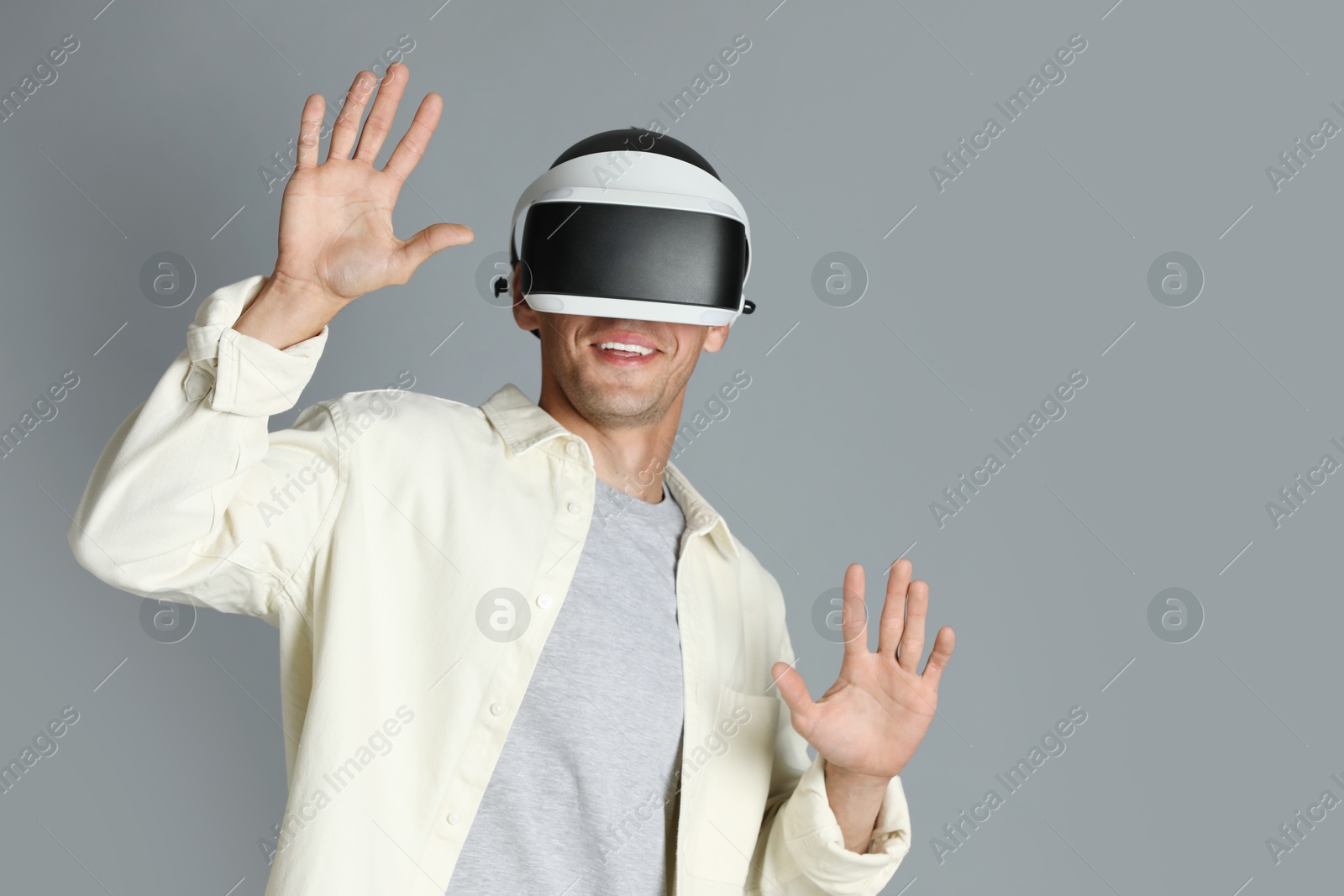 Photo of Smiling man using virtual reality headset on gray background, space for text