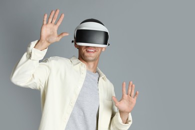 Smiling man using virtual reality headset on gray background, space for text