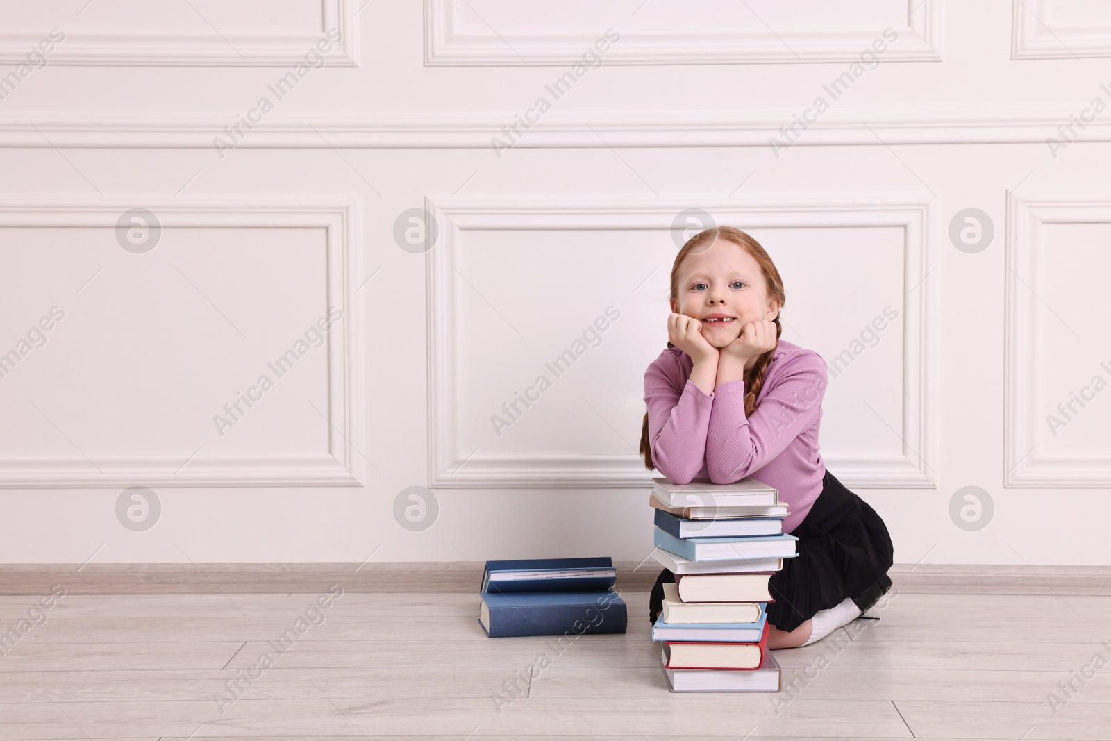 Photo of Smiling girl with stack of books indoors. Space for text