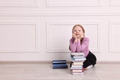 Smiling girl with stack of books indoors. Space for text