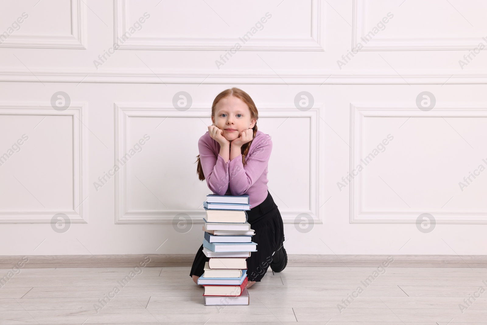 Photo of Little girl with stack of books on floor indoors