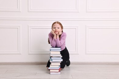 Little girl with stack of books on floor indoors