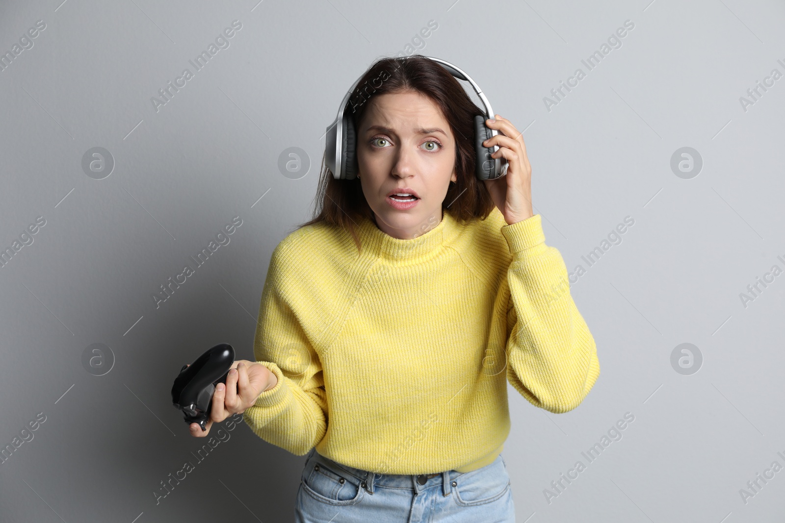 Photo of Confused woman in headphones with game controller on light grey background