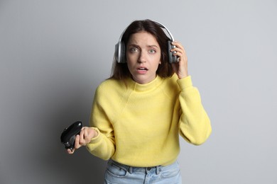 Confused woman in headphones with game controller on light grey background