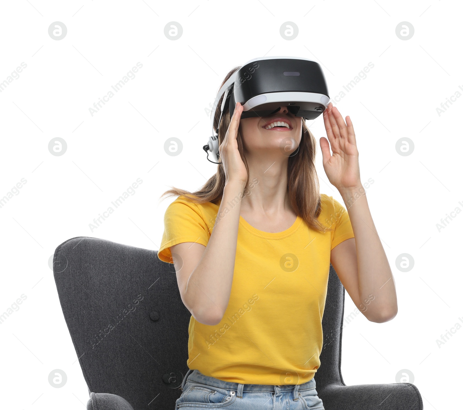 Photo of Smiling woman using virtual reality headset while sitting in armchair against white background