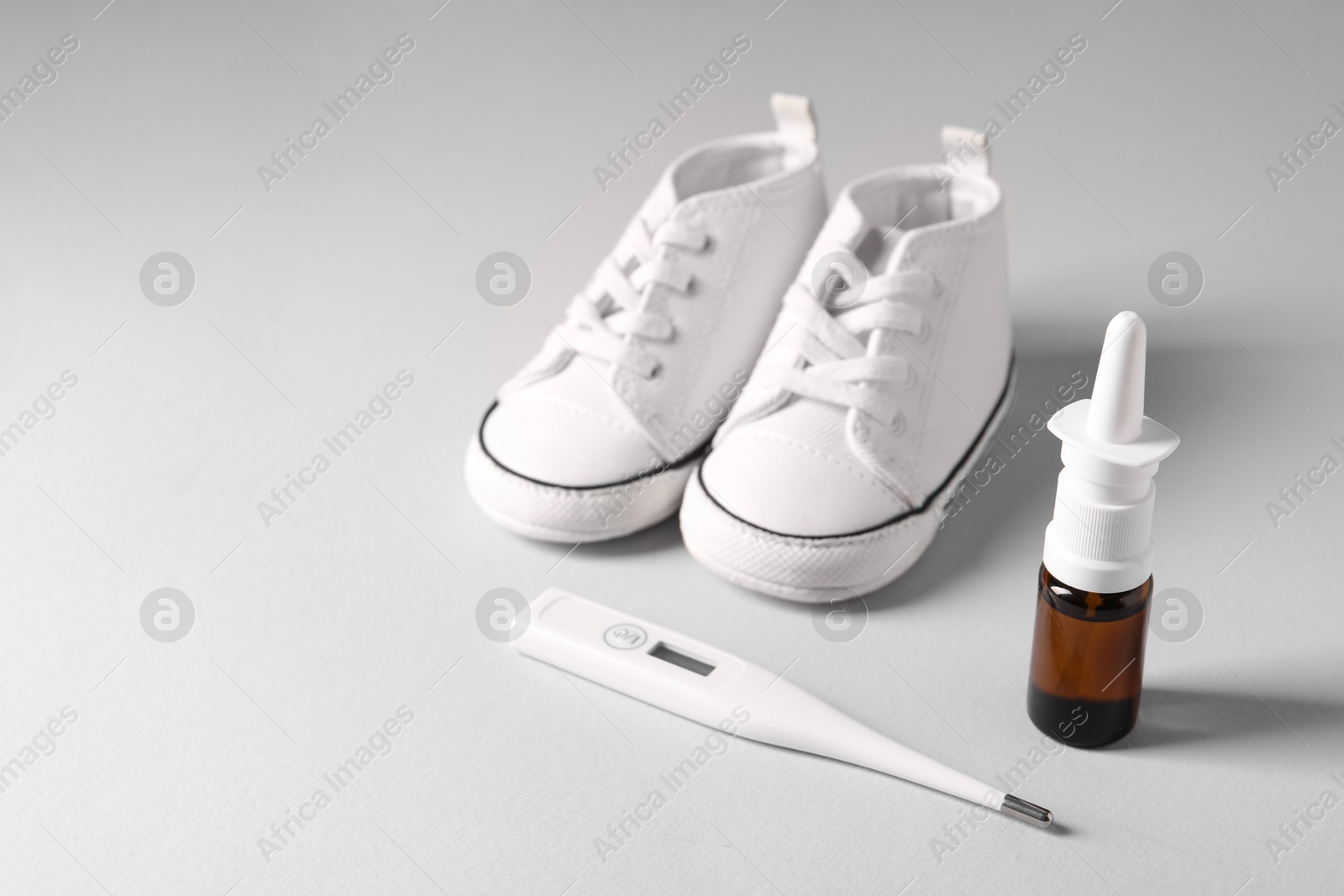 Photo of Child`s sneakers, thermometer and nasal spray on grey table, closeup. Space for text