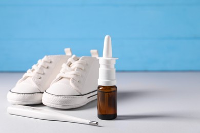 Photo of Child`s sneakers, thermometer and nasal spray on grey table, closeup. Space for text