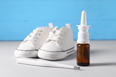 Photo of Child`s sneakers, thermometer and nasal spray on grey table, closeup