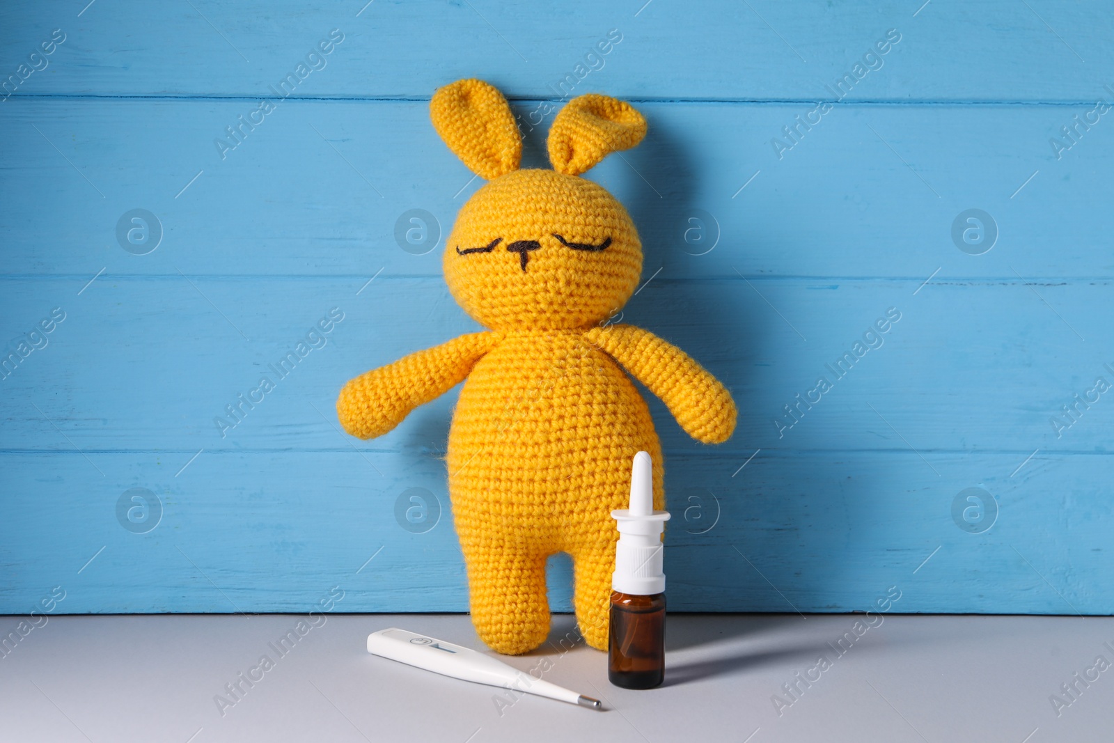 Photo of Toy bunny with nasal spray and thermometer on grey table near light blue wooden wall