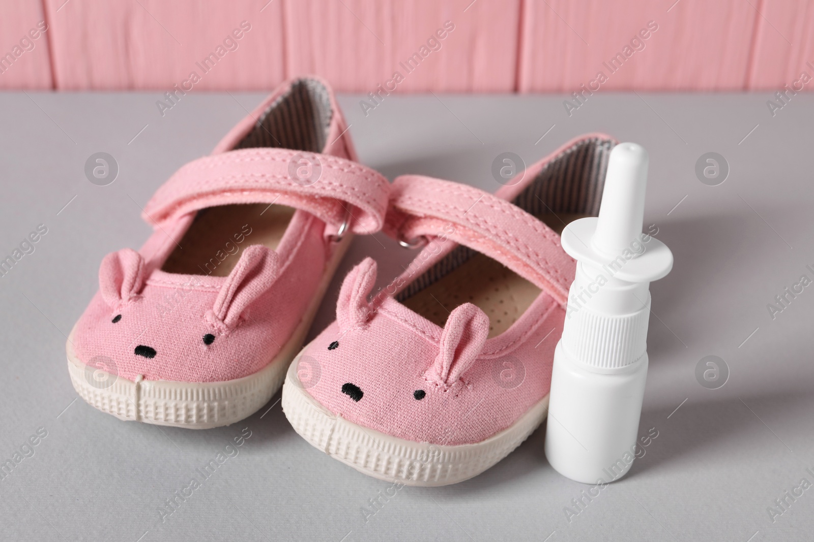 Photo of Cute baby shoes and nasal spray on grey table, closeup