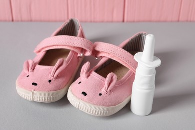 Cute baby shoes and nasal spray on grey table, closeup