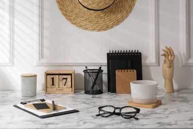 Photo of Stylish office workplace. Decor elements, glasses, cup and stationery on marble table near white wall