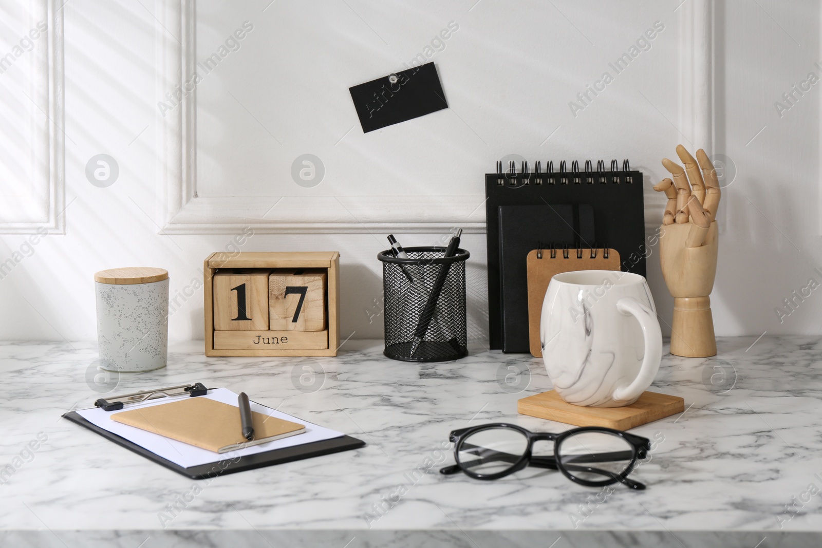 Photo of Stylish office workplace. Decor elements, glasses, cup and stationery on marble table near white wall