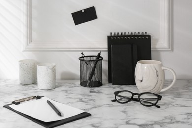 Photo of Stylish office workplace. Decor elements, glasses, cup and stationery on marble table near white wall