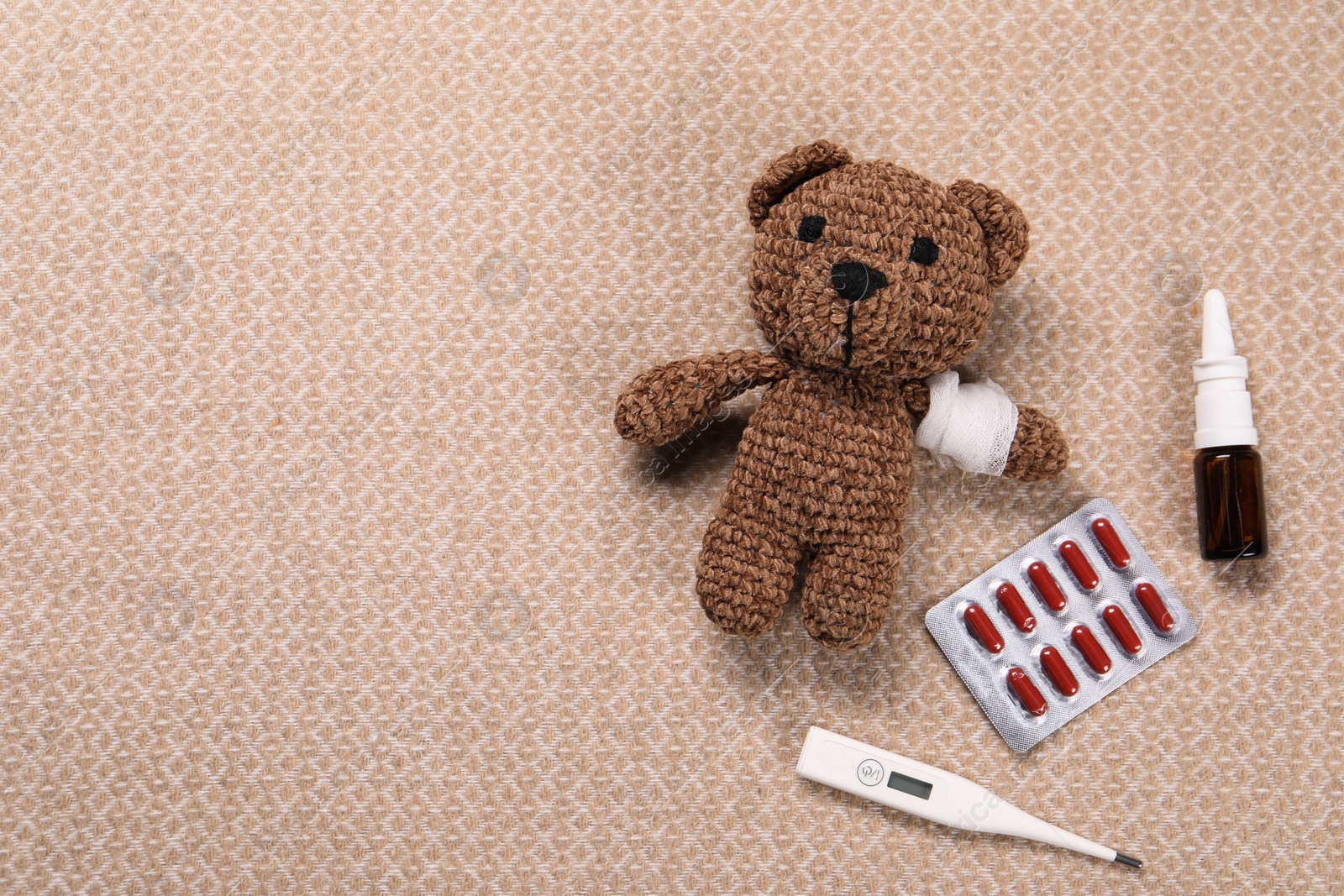 Photo of Toy bear with bandage, thermometer, pills and nasal spray on blanket, flat lay. Space for text