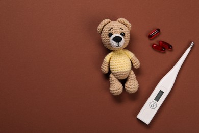 Photo of Toy bear, thermometer and pills on brown background, flat lay. Space for text