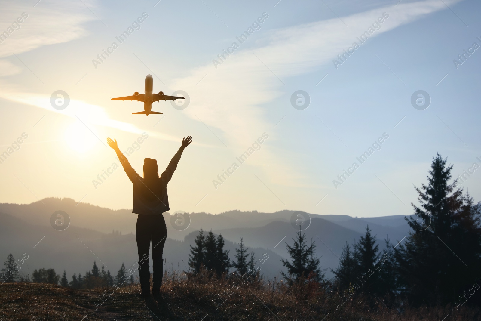 Image of Woman looking at airplane flying in sky over mountains during sunrise, back view