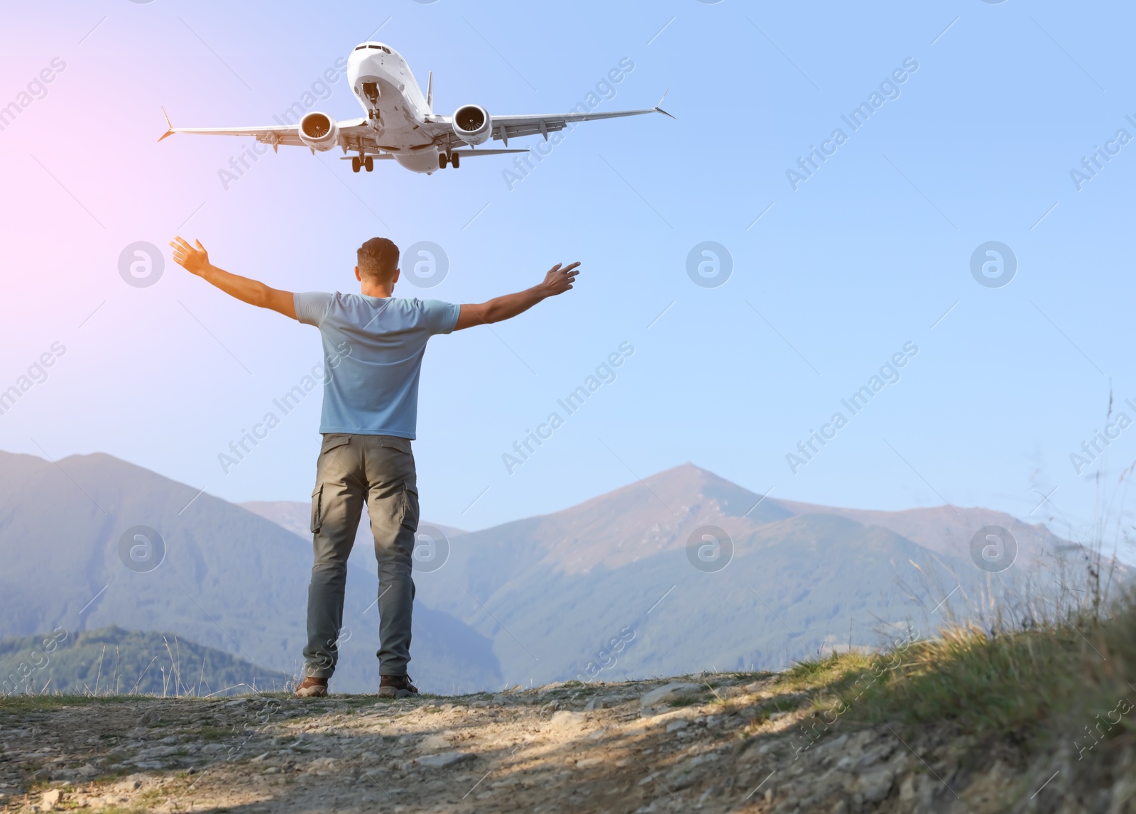 Image of Man looking at airplane flying in sky over mountains during sunrise, back view