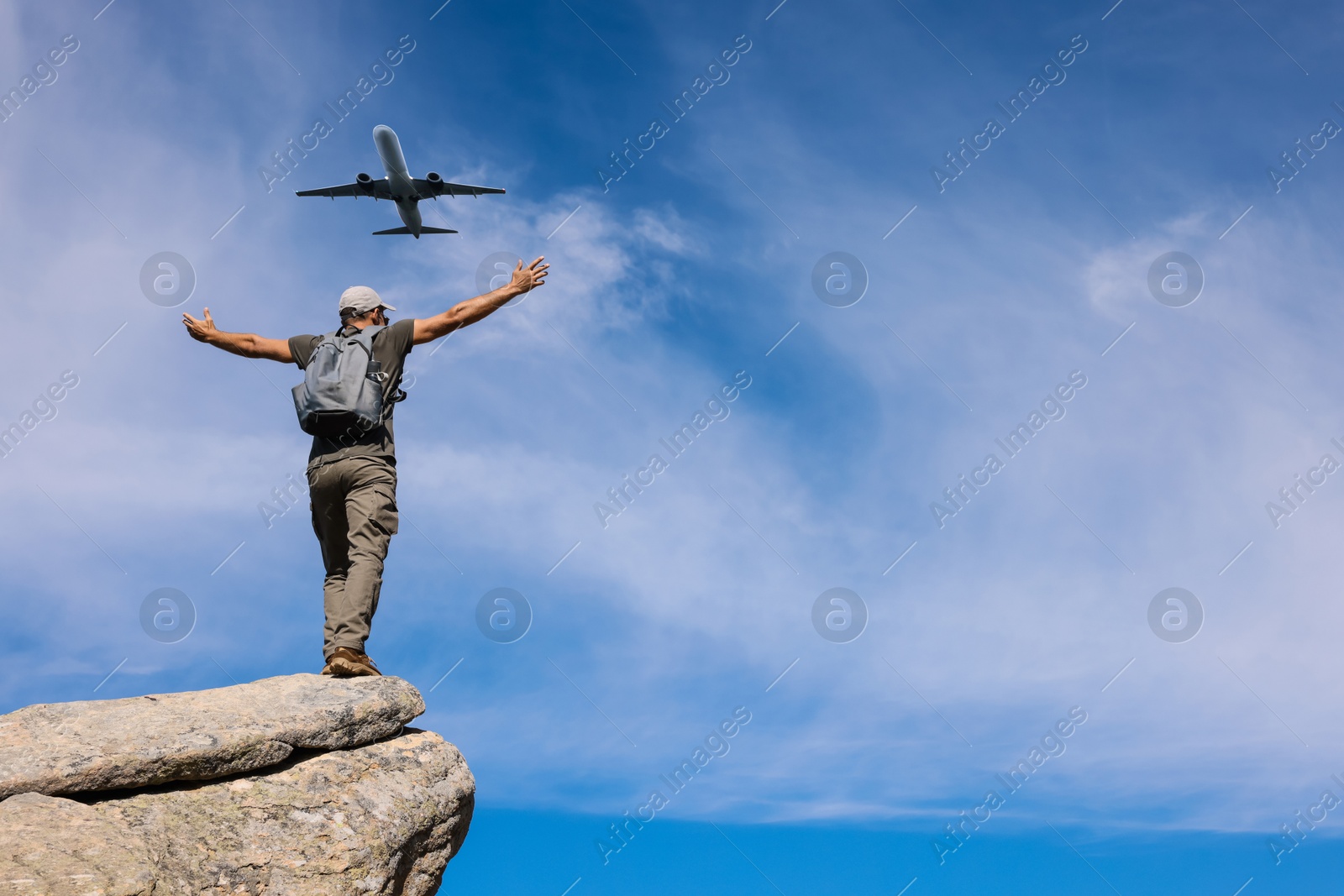 Image of Man on cliff looking at airplane flying in sky