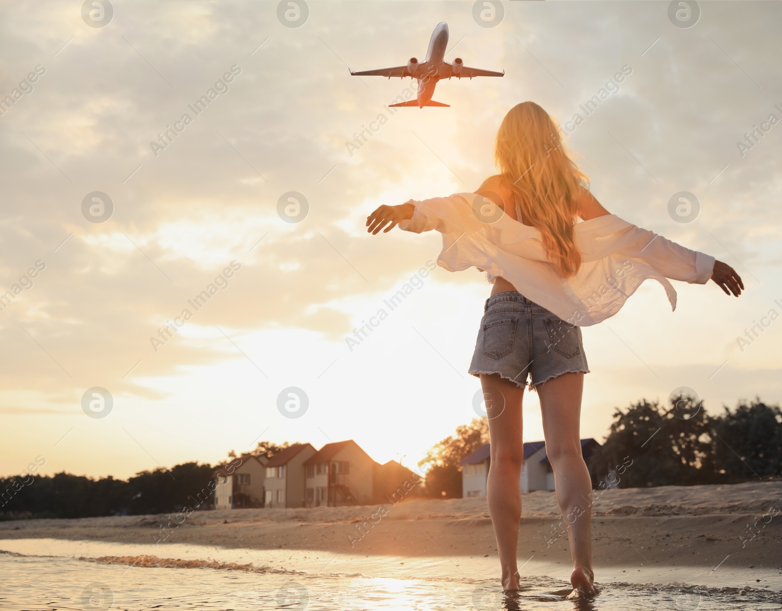 Image of Woman on beach looking at airplane flying in sunset sky, back view