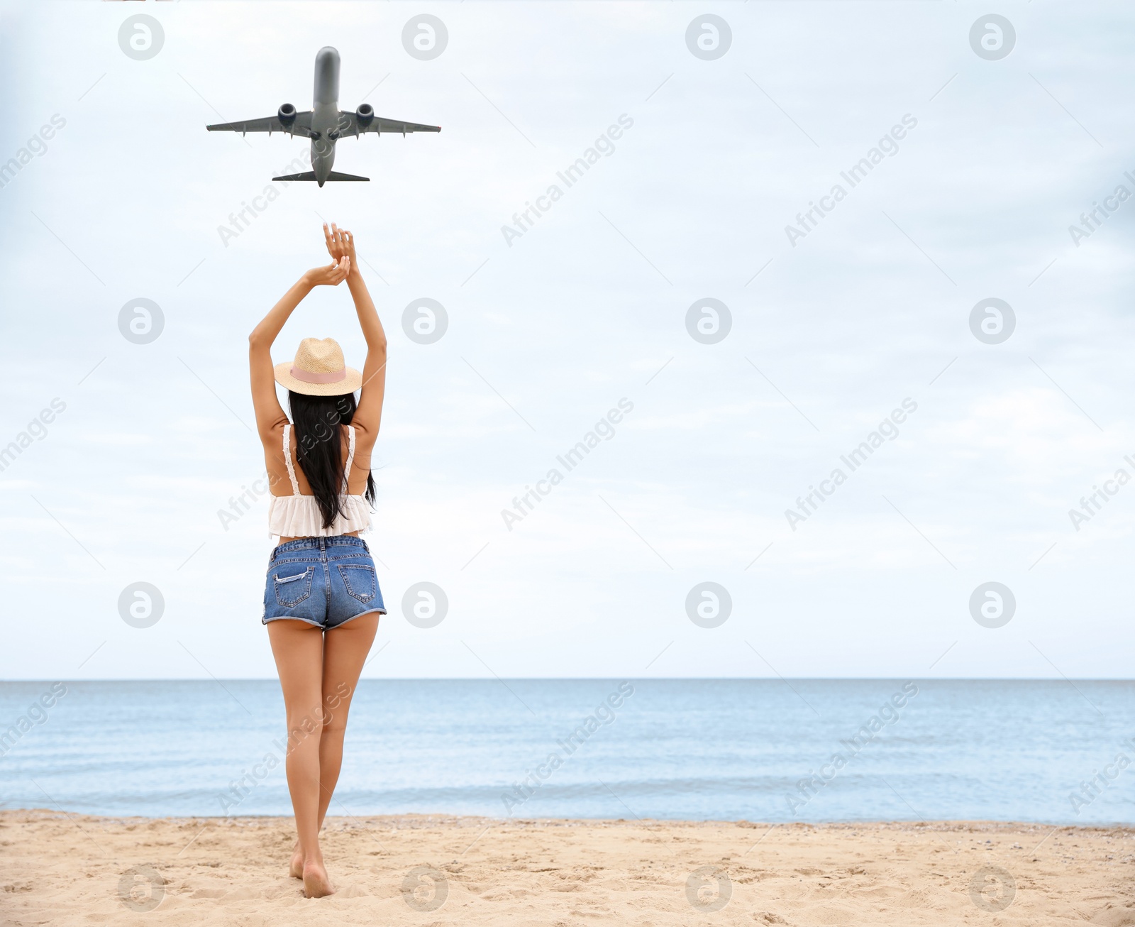 Image of Woman on beach looking at airplane flying in sky, back view