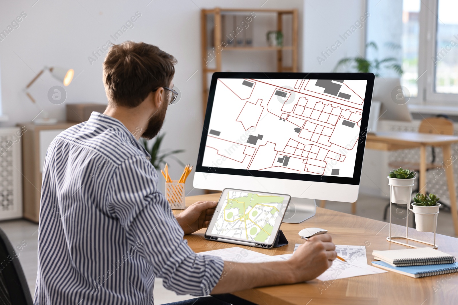 Image of Man working with cadastral map on tablet and computer at table in office