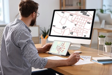 Image of Man working with cadastral map on tablet and computer at table in office