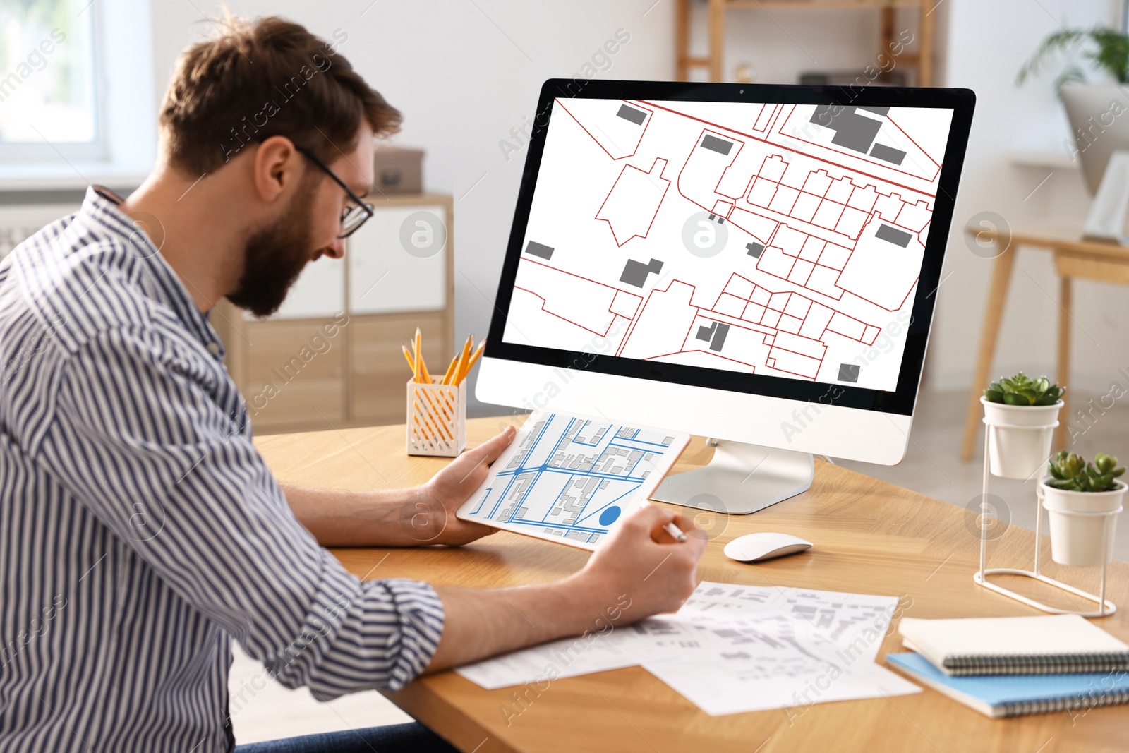 Image of Man working with cadastral map on tablet and computer at table in office