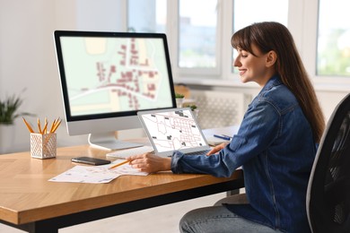 Woman working with cadastral map on computers at table in office