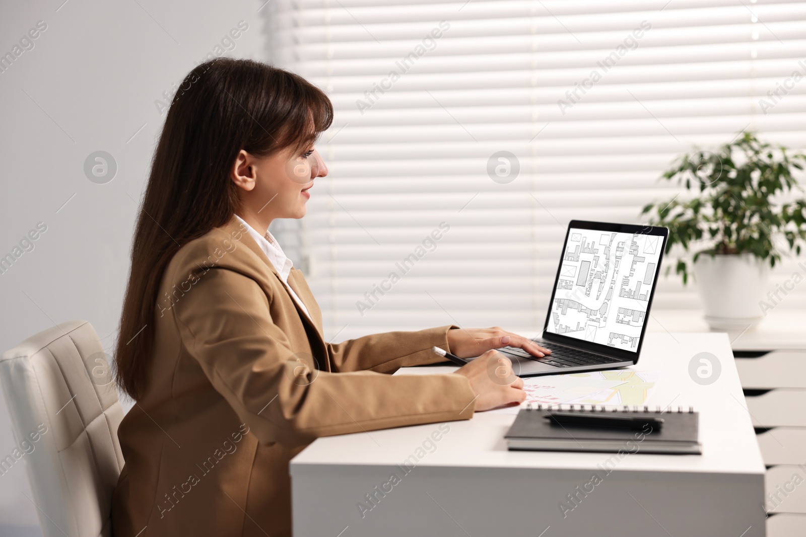 Image of Woman working with cadastral map on laptop at table in office