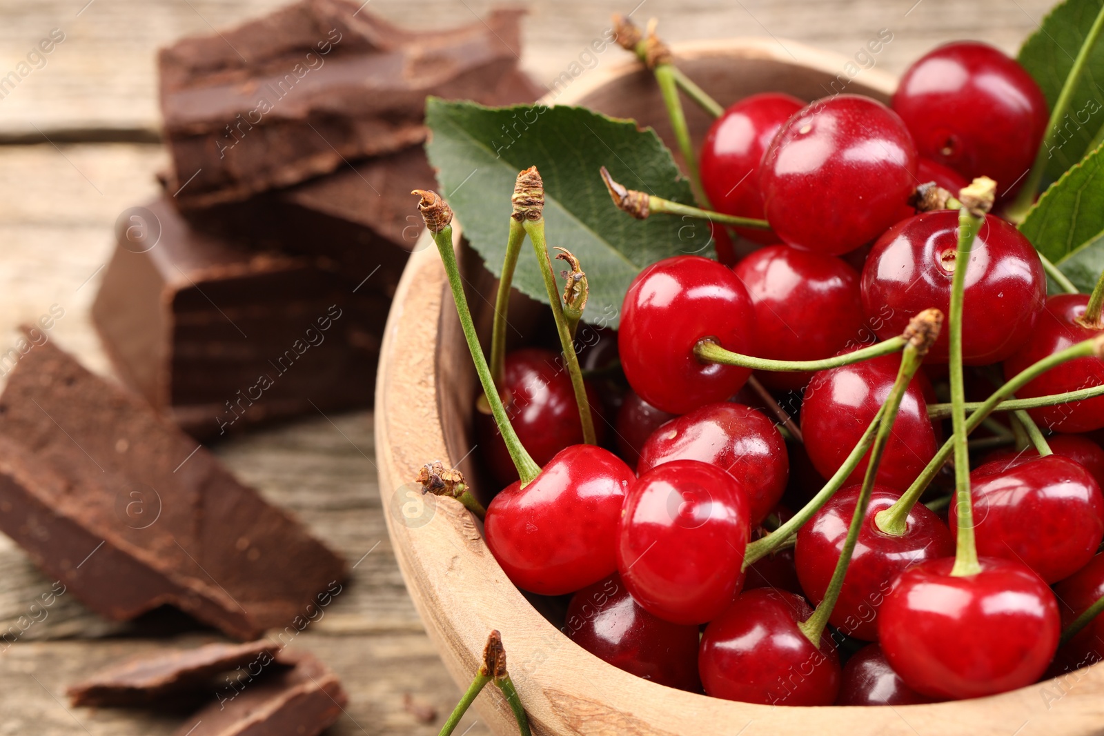 Photo of Fresh cherries with green leaves in bowl on table, closeup