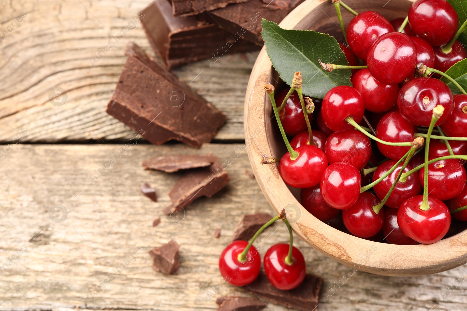 Photo of Fresh cherries in bowl and dark chocolate on wooden table, above view. Space for text