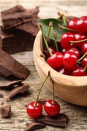 Photo of Fresh cherries in bowl and dark chocolate on wooden table, closeup