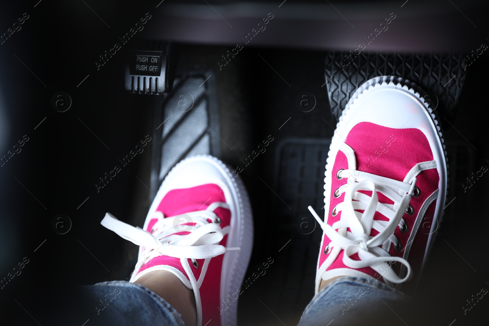 Photo of Woman in sneakers pushing on pedal of car brake, closeup