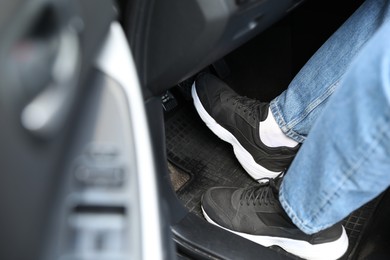 Photo of Man in sneakers pushing on pedal of car brake, closeup