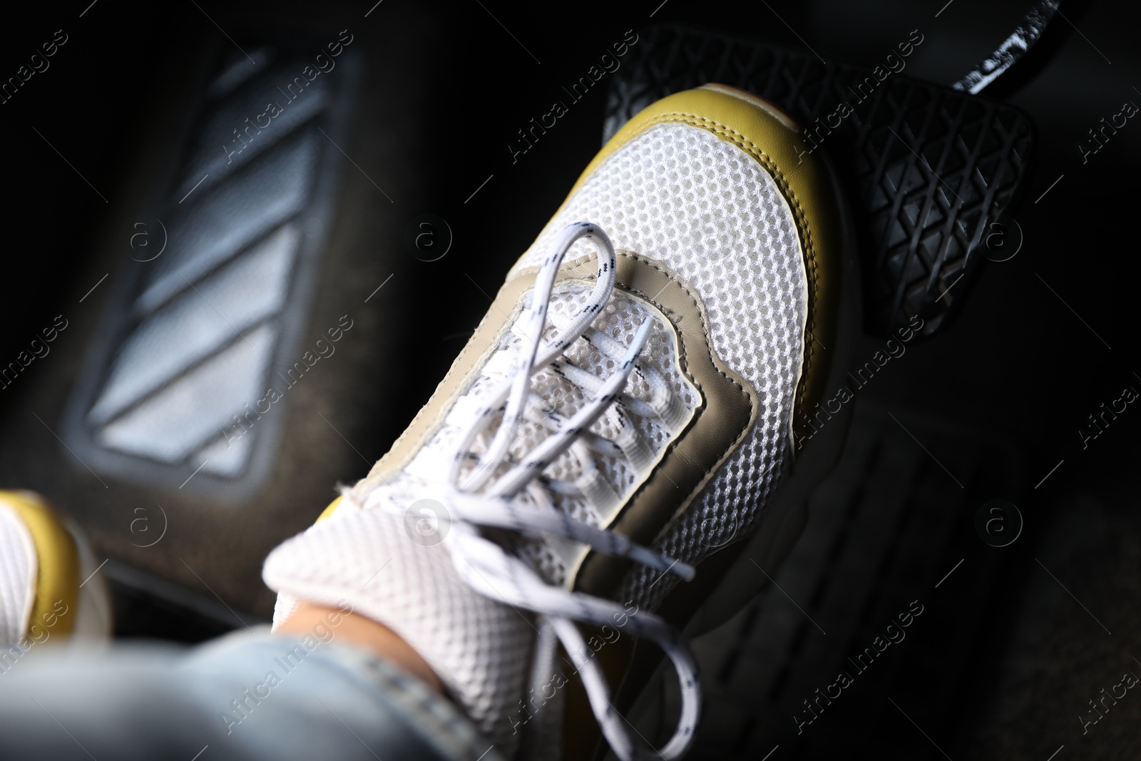 Photo of Woman in sneakers pushing on pedal of car brake, closeup