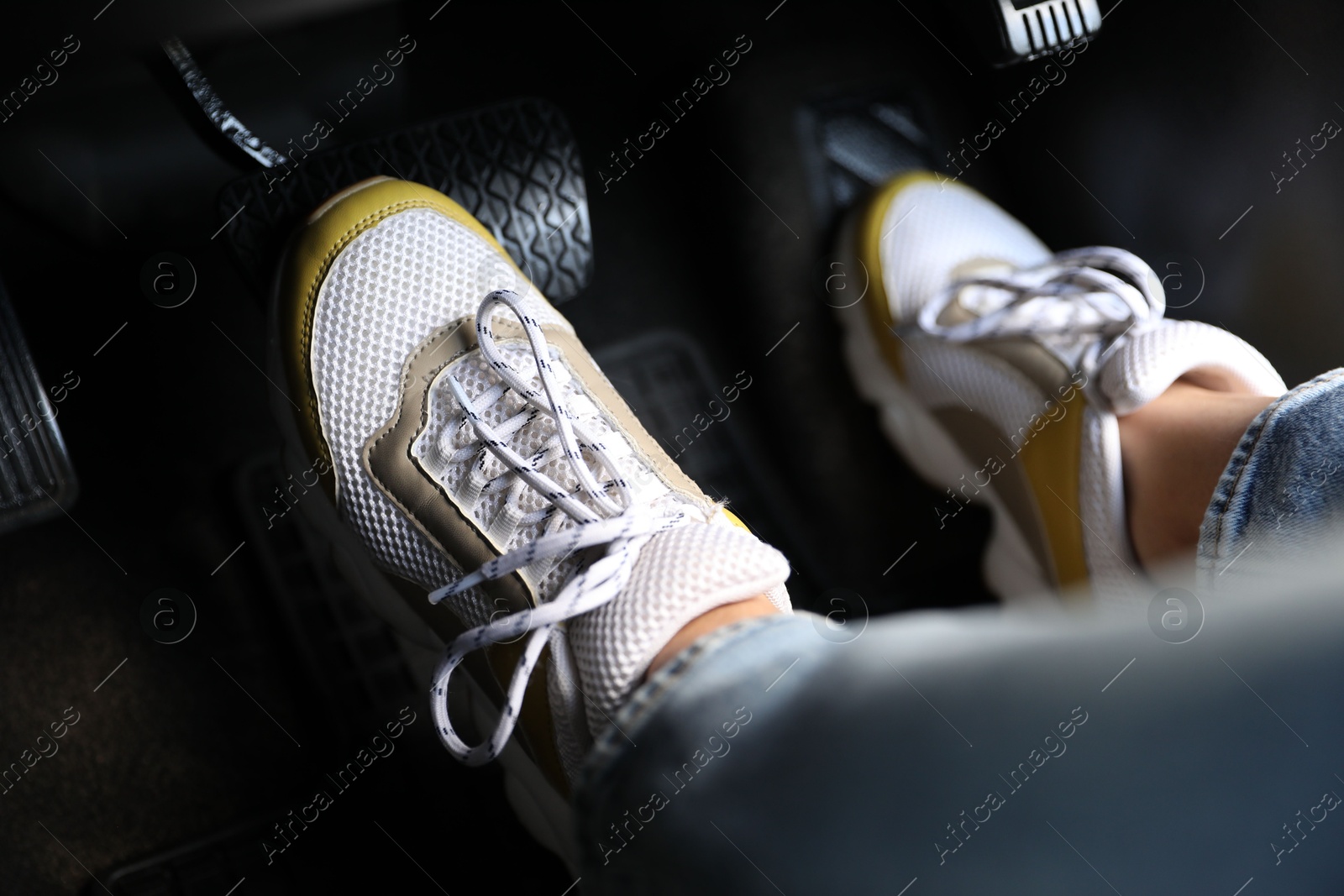 Photo of Woman in sneakers pushing on pedal of car brake, closeup