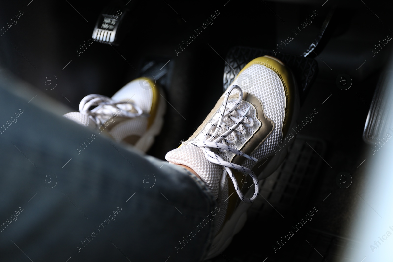 Photo of Woman in sneakers pushing on pedal of car brake, closeup