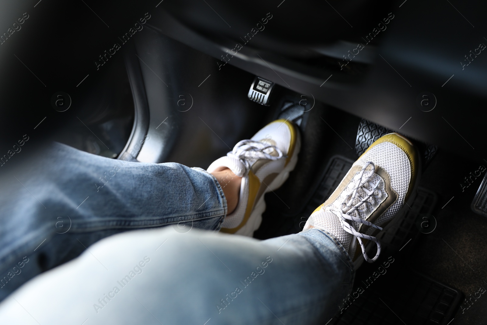 Photo of Woman in sneakers pushing on pedal of car brake, closeup