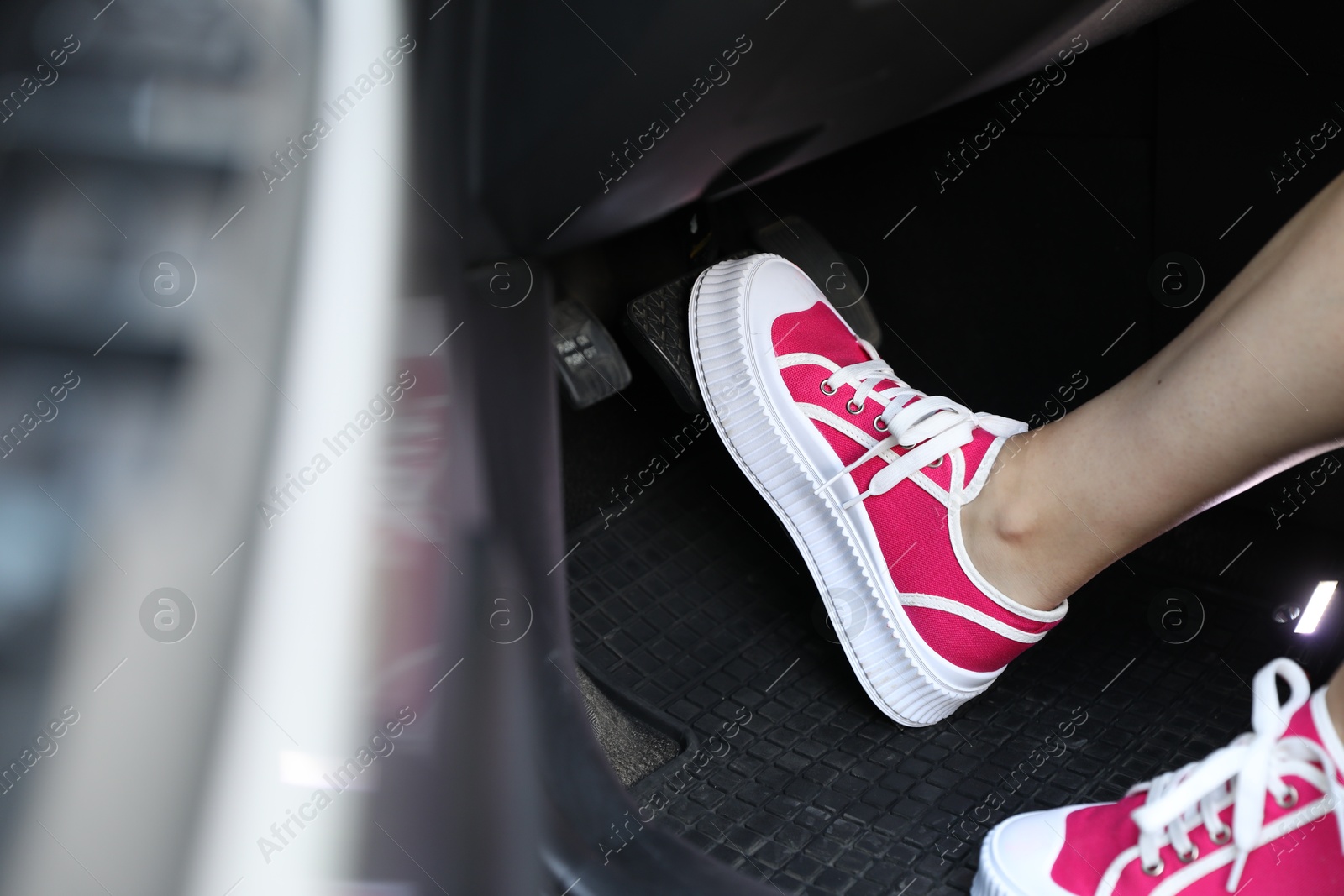 Photo of Woman in sneakers pushing on pedal of car brake, closeup