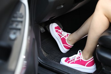 Photo of Woman in sneakers pushing on pedal of car brake, closeup