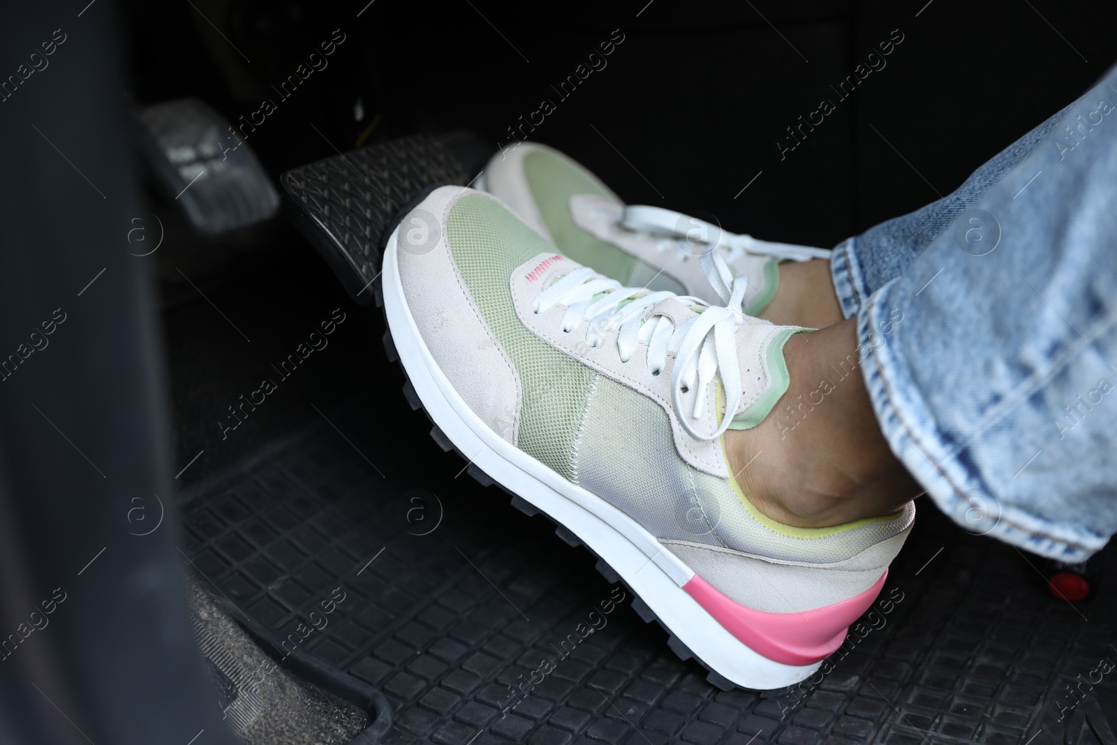 Photo of Woman in sneakers pushing on pedal of car brake, closeup