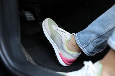 Photo of Woman in sneakers pushing on pedal of car brake, closeup