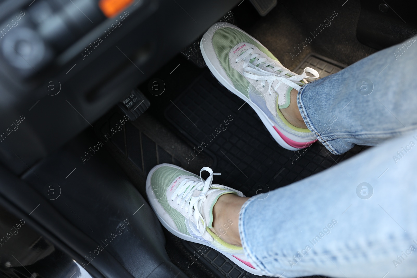 Photo of Woman in sneakers pushing on pedal of car brake, closeup