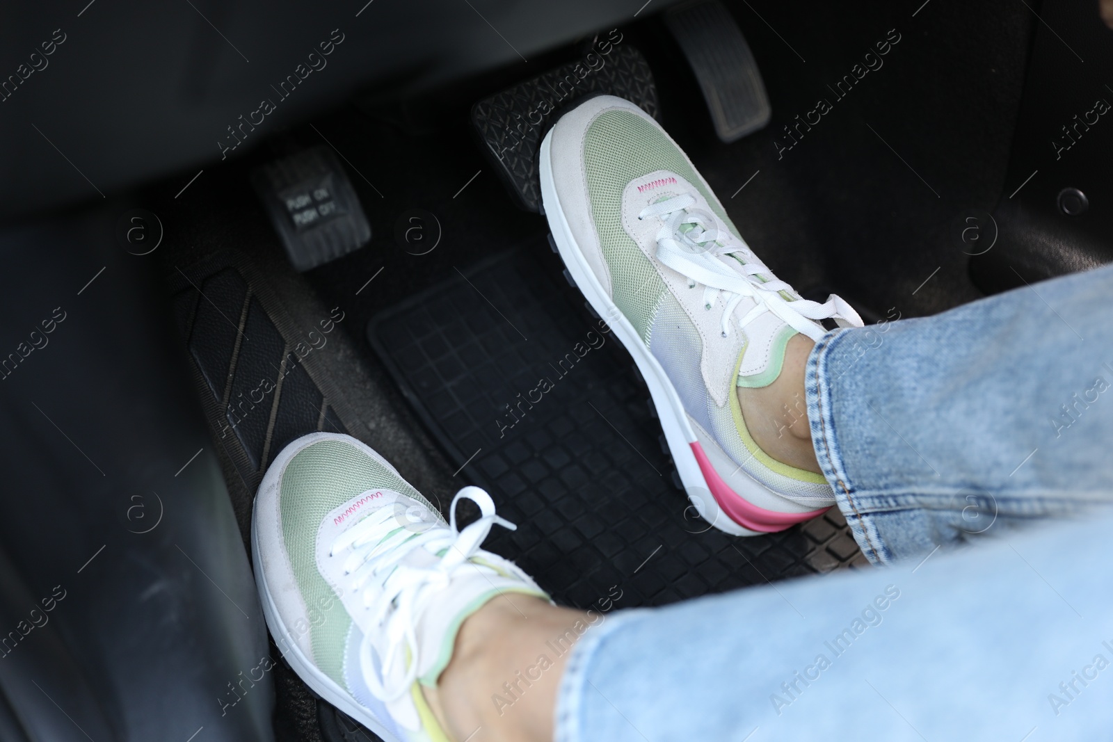 Photo of Woman in sneakers pushing on pedal of car brake, closeup