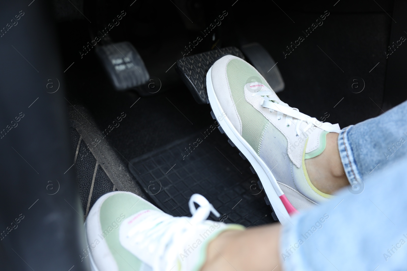 Photo of Woman in sneakers pushing on pedal of car brake, closeup