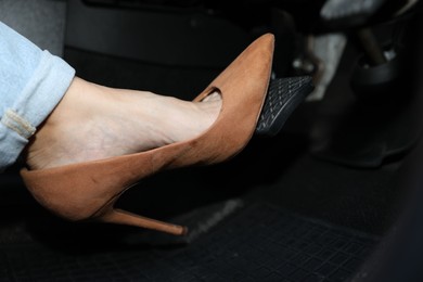 Photo of Woman in high heels pushing on pedal of car brake, closeup