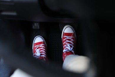 Photo of Woman in sneakers pushing on pedal of car brake, closeup