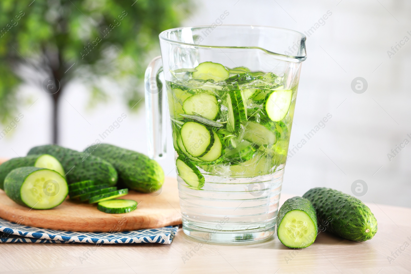 Photo of Refreshing cucumber water in jug and vegetables on light wooden table, closeup