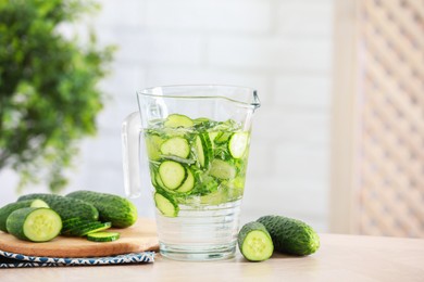 Refreshing cucumber water in jug and vegetables on light wooden table. Space for text